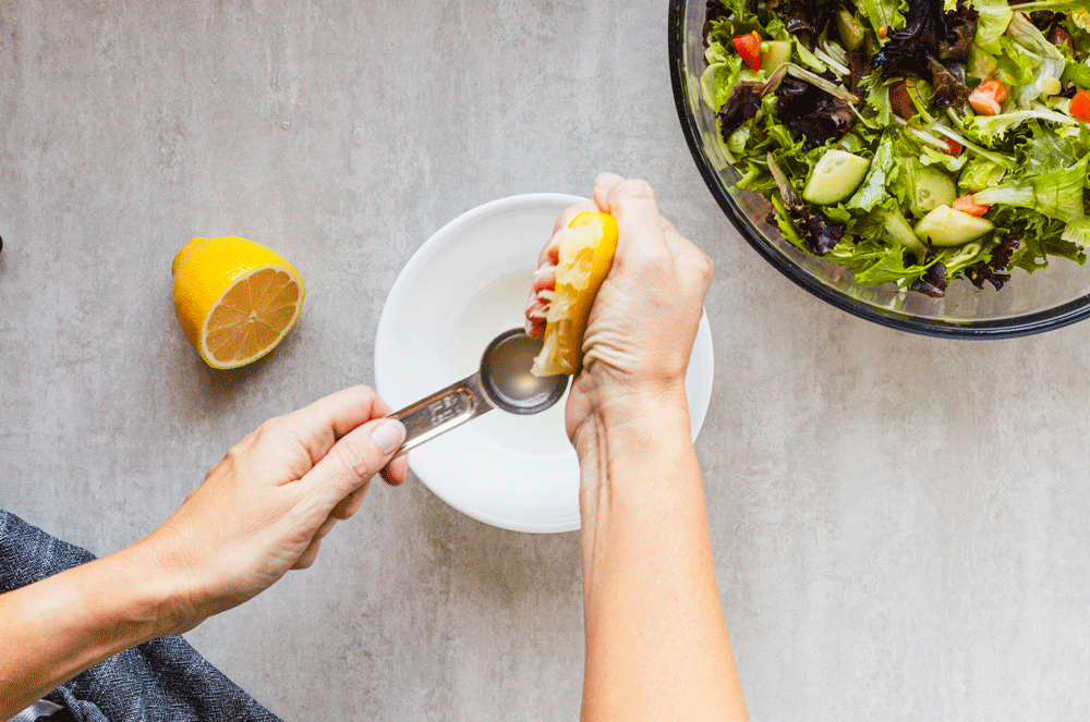 Squeezing lemon juice into bowl beside fresh salad.