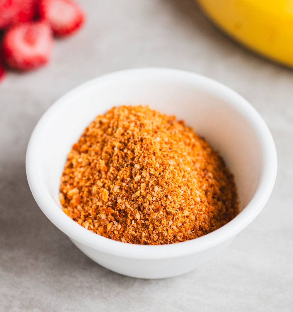Seasoned breadcrumbs in a white bowl with fruit nearby.