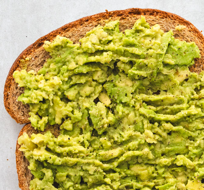 Mashed avocado spread on whole-grain toast slice.