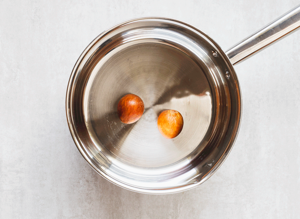 Avocado pits soaking in a stainless steel pot.