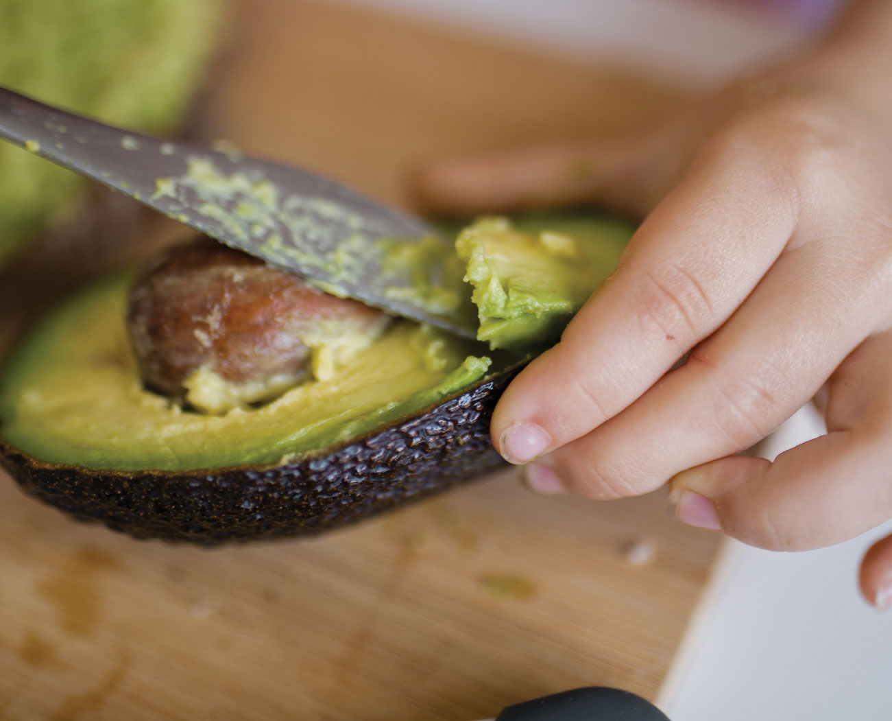 Child scooping avocado flesh with a knife.