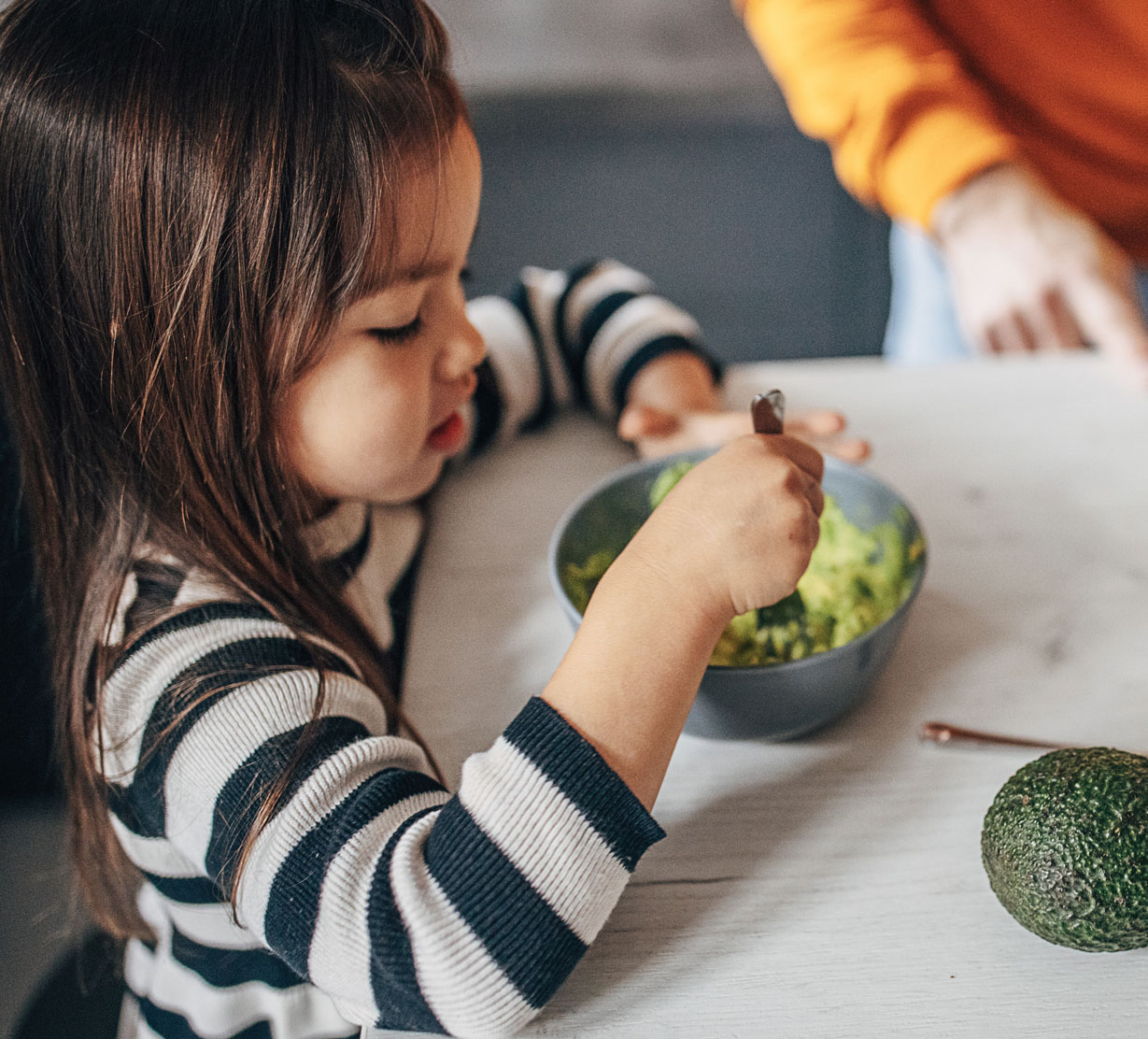 Child mashing avocados with fork in bowl.