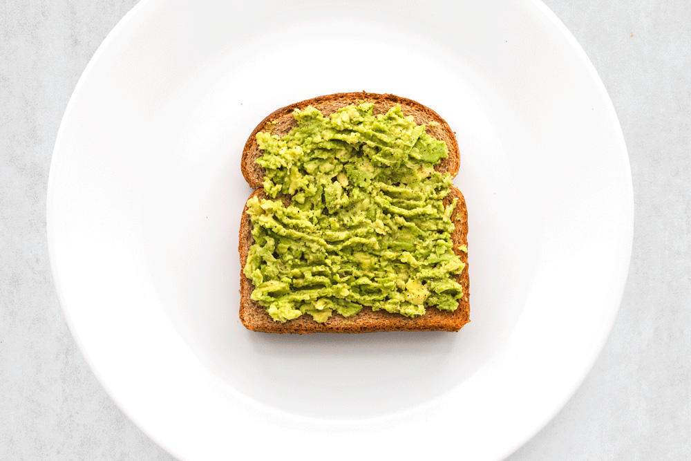 Toast with mashed avocado on white plate.