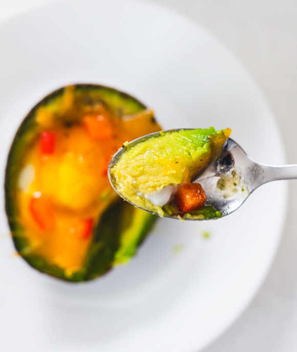 Avocado stuffed with cheese and vegetables on spoon.