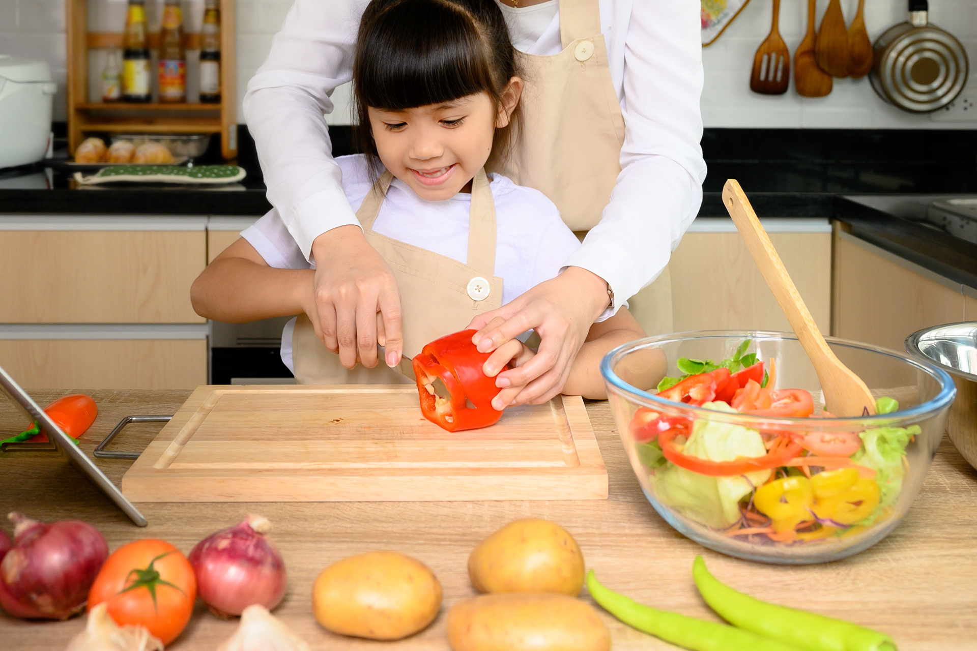 Child and adult slicing red bell pepper together.