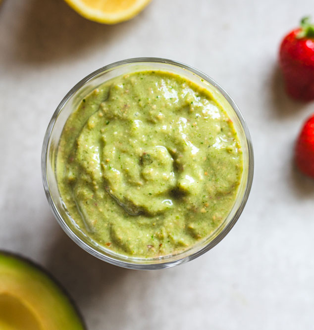 Green smoothie in glass with strawberries and lemon.