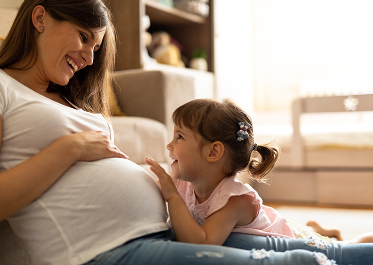 Pregnant woman and child smiling, touching belly.