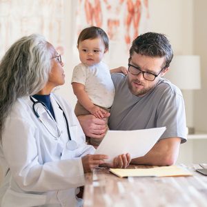Doctor discusses paperwork with father holding toddler.