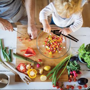 Child and adult preparing vegetables together at table.