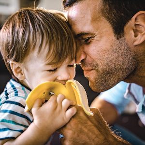Father and child sharing banana moment, smiling closely.