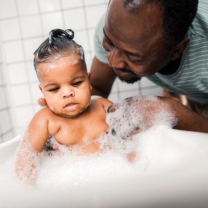 Father bathing baby in soapy bathtub.