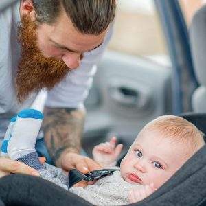 Bearded man securing baby in car seat.