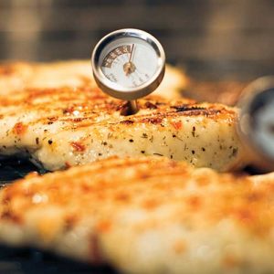 Grilled chicken breast with a meat thermometer inserted.