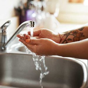 Hands washing under kitchen faucet water flow.