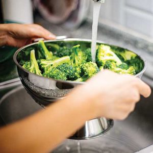Washing fresh broccoli in a kitchen sink.