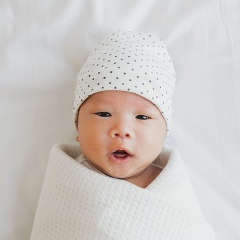 birth-baby Swaddled baby with polka dot hat, looking surprised.