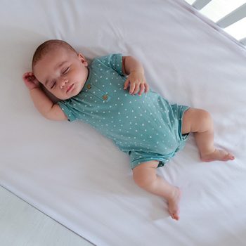 sleeps-baby Baby peacefully sleeping in teal onesie on bed.