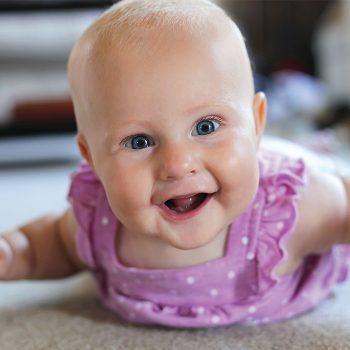 smilingbaby Smiling baby in a purple dress on floor.